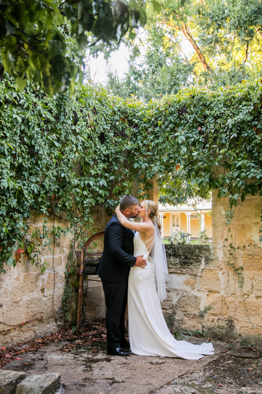 Tim and Natalia Exelby Bride and groom kissing under overgrowth