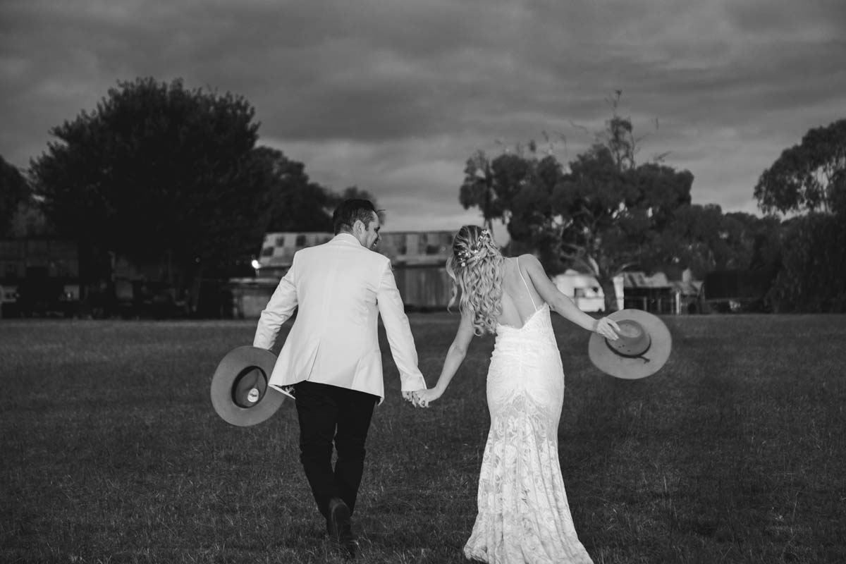 Wedding Photography bride and groom walking away with hats in hand